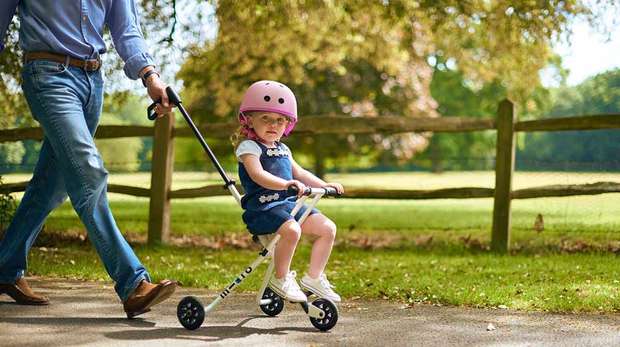 Little girl riding Micro Trike at Whipsnade Zoo pushed by dad in jeans