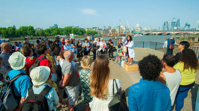 Photo of a Soapbox Science presenter and crowd by the Thames with London skyline in background