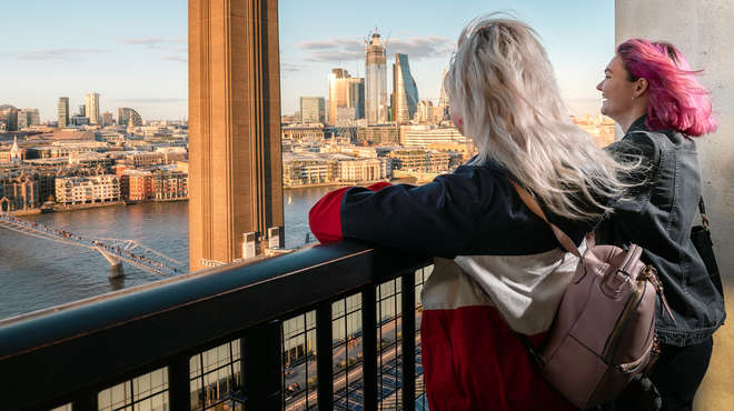 Two girls looking over a balcony at blue sky in central London