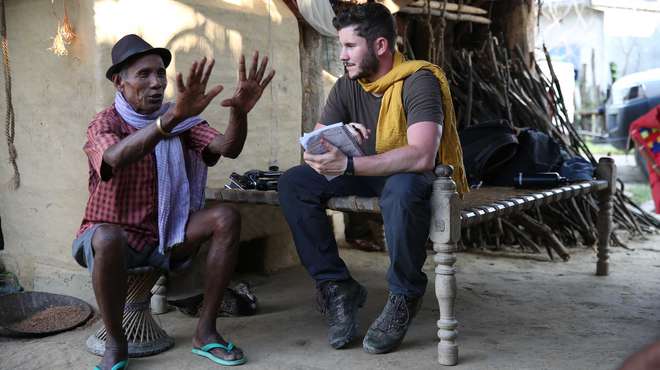 journalist talking to man in hat in a village hut in nepal