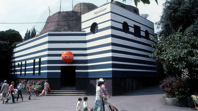 1980's photo of our aquarium building, woman walks past with two children and buggy in front of aquarium entrance