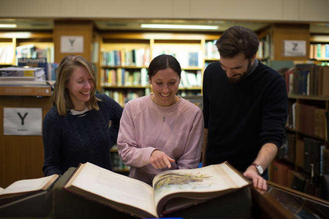 3 visitors admiring a large historic book in ZSL Library