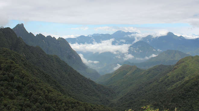 Wide angle landscape photograph looking down a valley with cloud-wreathed mountains in the background  