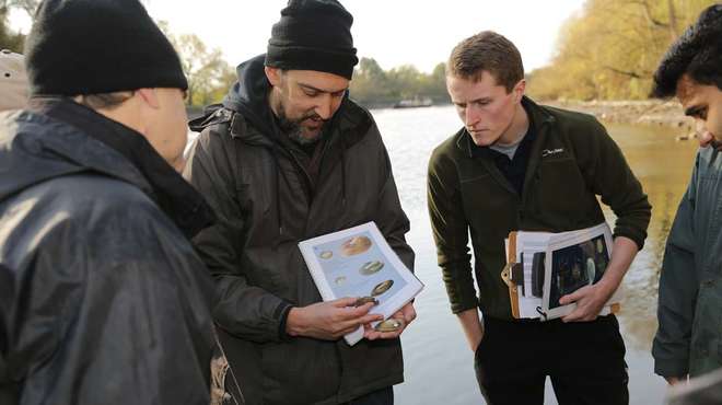 Photo - Joe with a group of volunteers by a river bank, comparing shellfish to a printed guide book