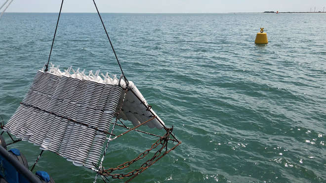 large white triangular device being lowered into calm seawater