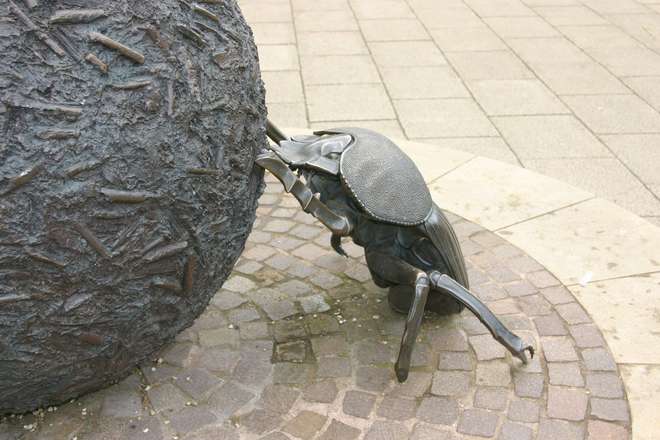 A sculpture of a bronze dung beetle rolling a large ball of dung