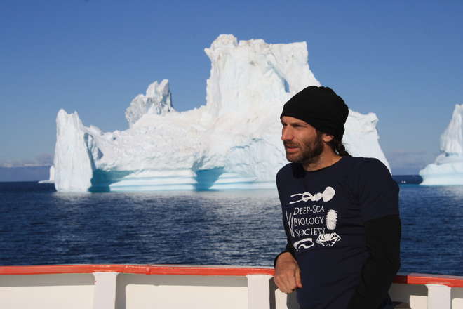 Chris Yesson on board a research vessel with icebergs in the background.
