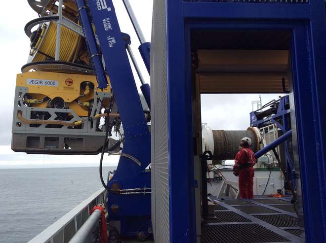 Photo of a large ROV (about the height of a person) being moved off the boat and into the sea.