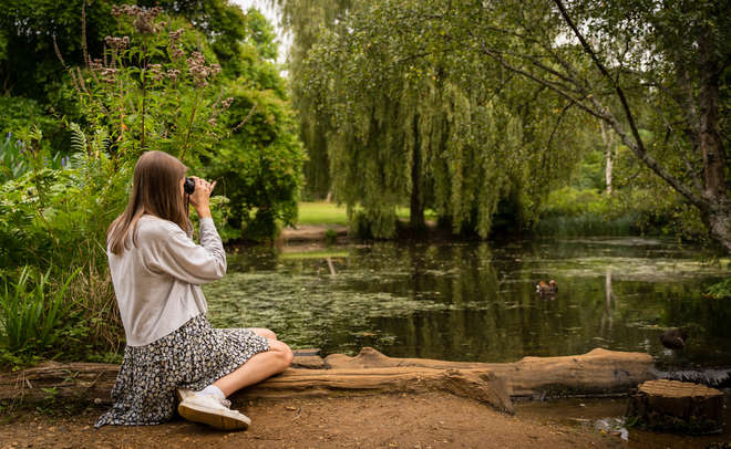 Biologist Camille Munday sits by the lake in Richmond park looking through a pair of binoculars