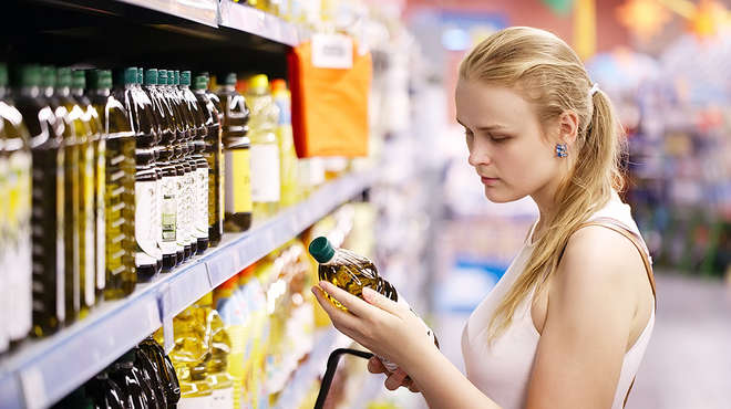 Woman in a supermarket looking at the label of a bottle of oil 